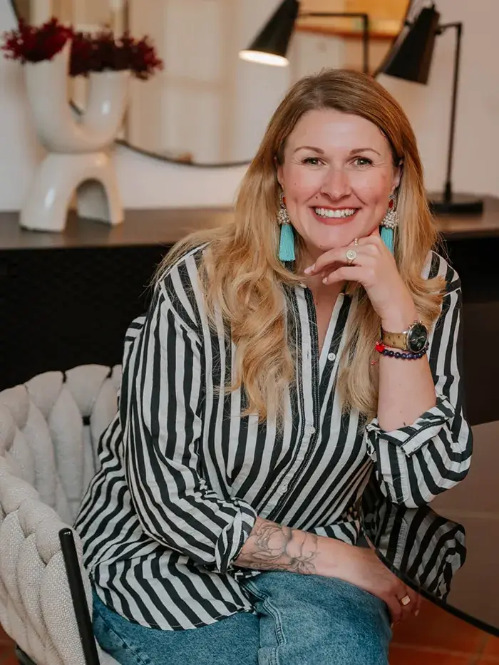 Immobilienmaklerin Anne lächelt in die Kamera und sitzt auf einem Stuhl